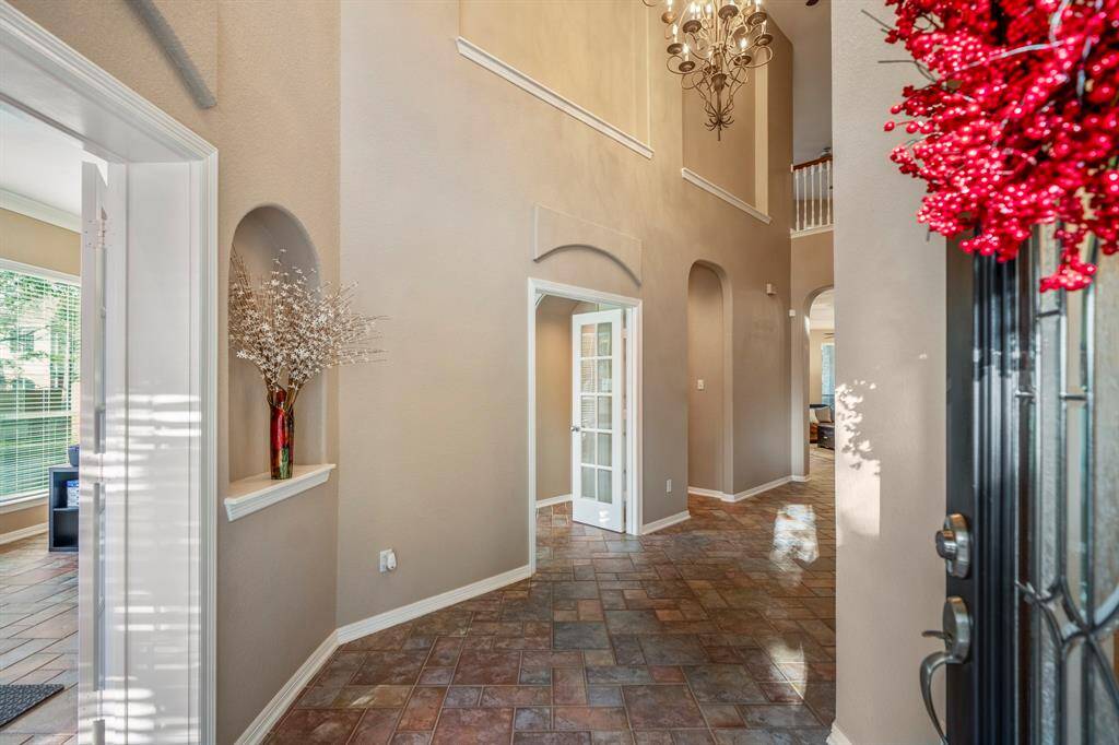Step inside to soaring two-story ceilings, a grand chandelier, and elegant arched insets. To the left, glass French doors open to the formal living room and one of 3 office areas, offering versatile spaces for work or relaxation. The open design provides a glimpse of the living room ahead and the loft-style game room above.