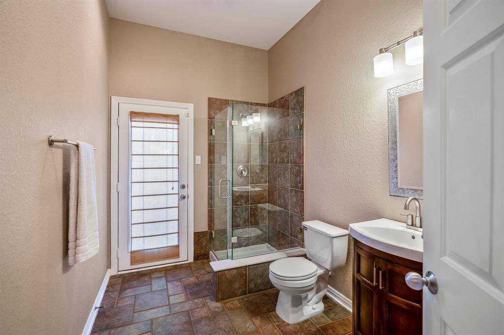 Across from the laundry room, this full bathroom features a frameless shower with a glass enclosure and tile flooring. A convenient door leads directly to the backyard, providing easy access from the bathroom to the outdoor space.