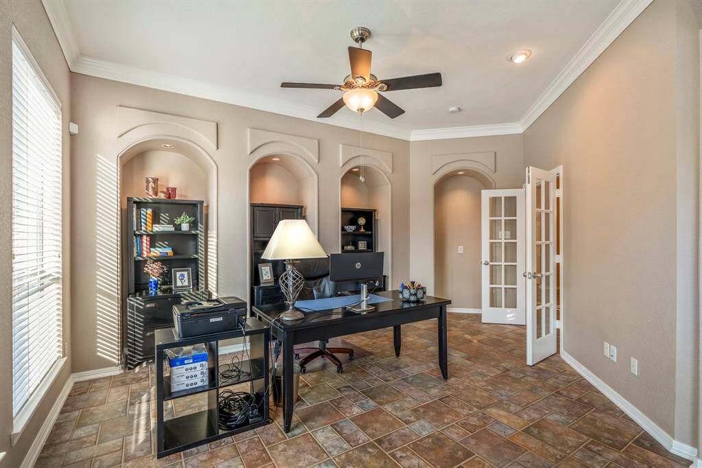 This spacious home office, the largest of three, offers a functional and elegant workspace. Recessed arches with built-in lighting provide the perfect spot for shelving or display, while large windows fill the room with natural light. French doors lead back to the foyer, and crown molding adds a refined touch.