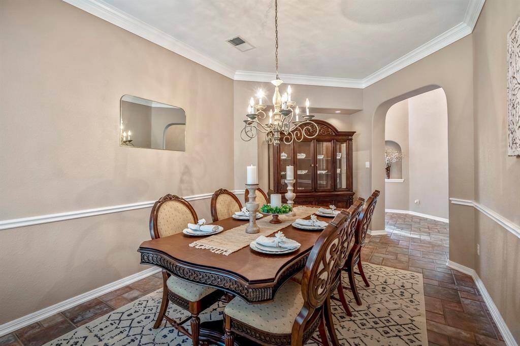 The formal dining room exudes elegance with double crown molding, a stylish chandelier, and a recessed, lit buffet area for added functionality. A chair rail enhances the classic design, while an arched entryway connects seamlessly to the foyer. Just out of view behind this angle, a secondary entrance and a doorway leading to the kitchen keep the space both beautiful and practical.