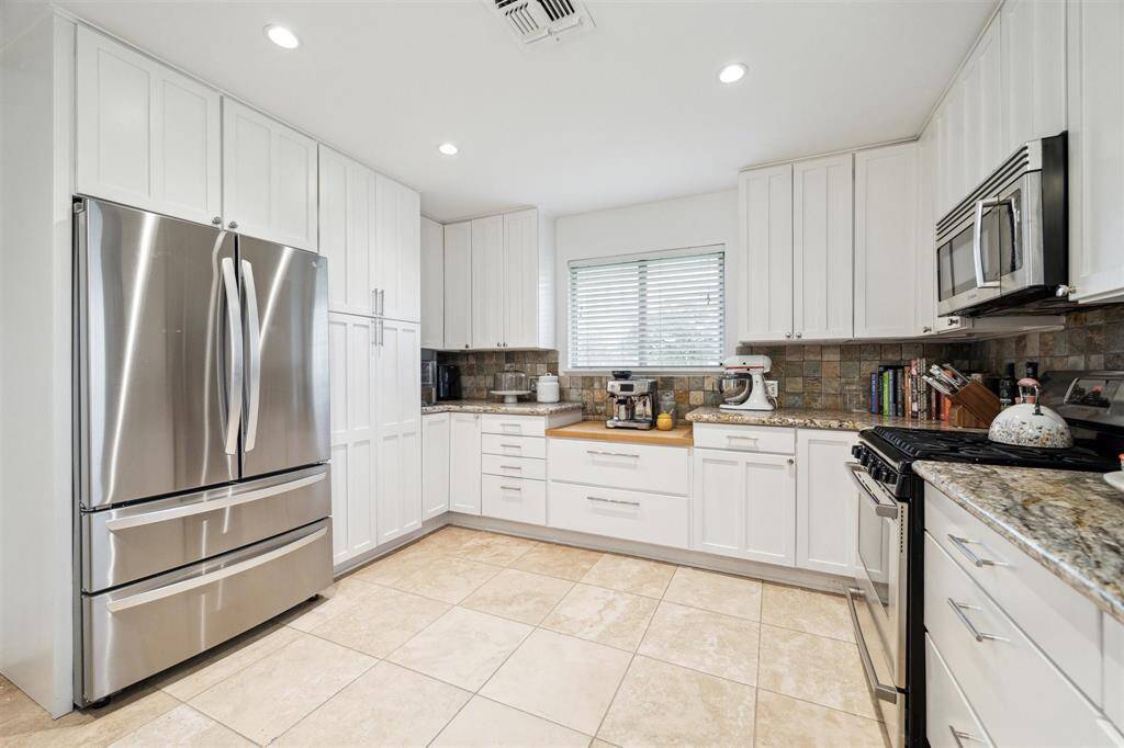 Plan your next culinary feat in this oversized kitchen featuring rows of floor-to-ceiling white cabinetry finished with granite countertops and tile backsplashes.