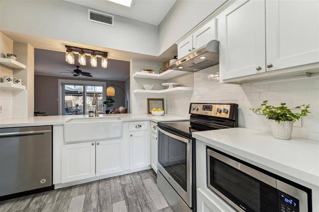 The beautiful kitchen boasts quartz countertops, open shelving, a subway tile backsplash, and sleek white cabinets.