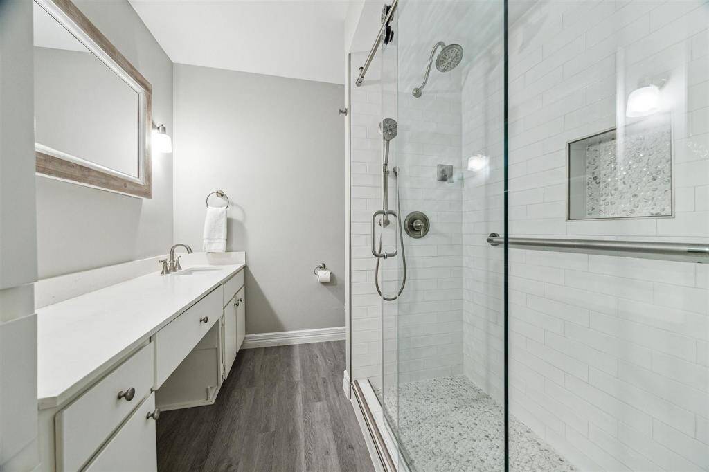 The primary bathroom offers a stunning shower with glass doors and beautiful tilework, complemented by a quartz countertop and vanity space.