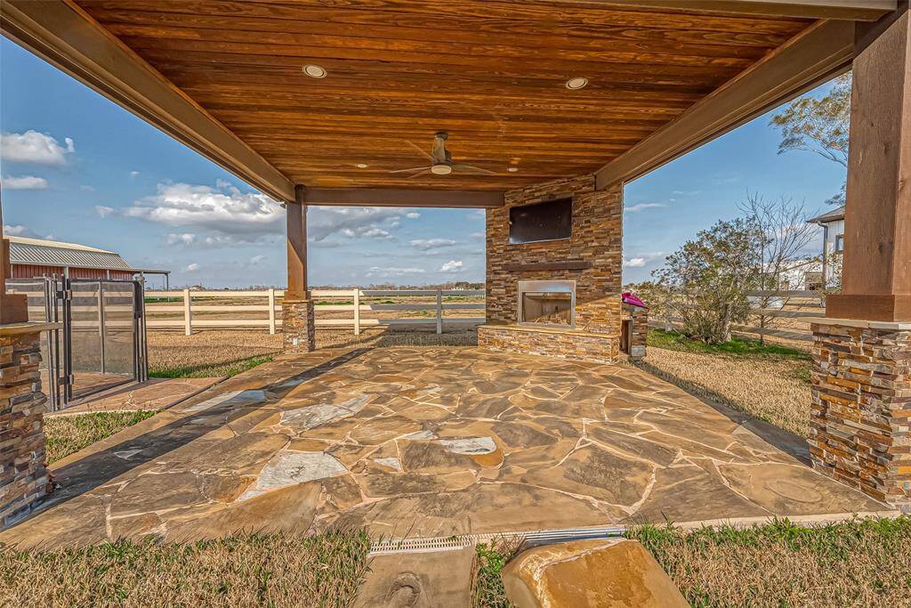 The exterior pavilion provides a perfect lounging spot with a cozy fireplace, recessed lighting, wood plank ceiling, and ceiling fan.