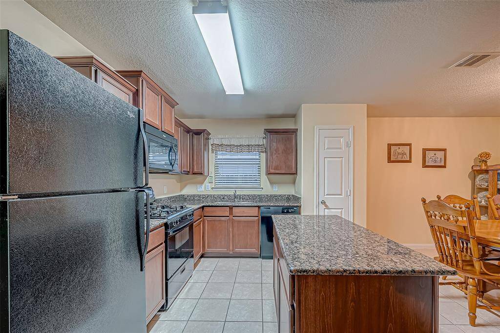 This kitchen features modern black appliances, ample dark wood cabinetry, and a spacious granite island. It's connected to a cozy dining area with room for a large dining table creating a warm and inviting space for cooking and entertaining.