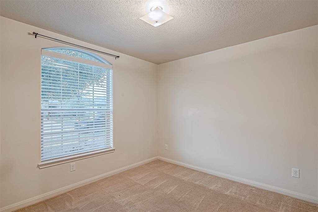 This is a bright, neutral-toned secondary room 1 featuring a large window with blinds, carpeted flooring.