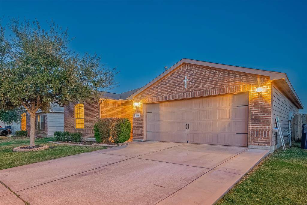 Charming single-story brick home with a two-car garage. Features a well-maintained front yard with a mature tree and neat landscaping. The warm exterior lighting creates an inviting ambiance.