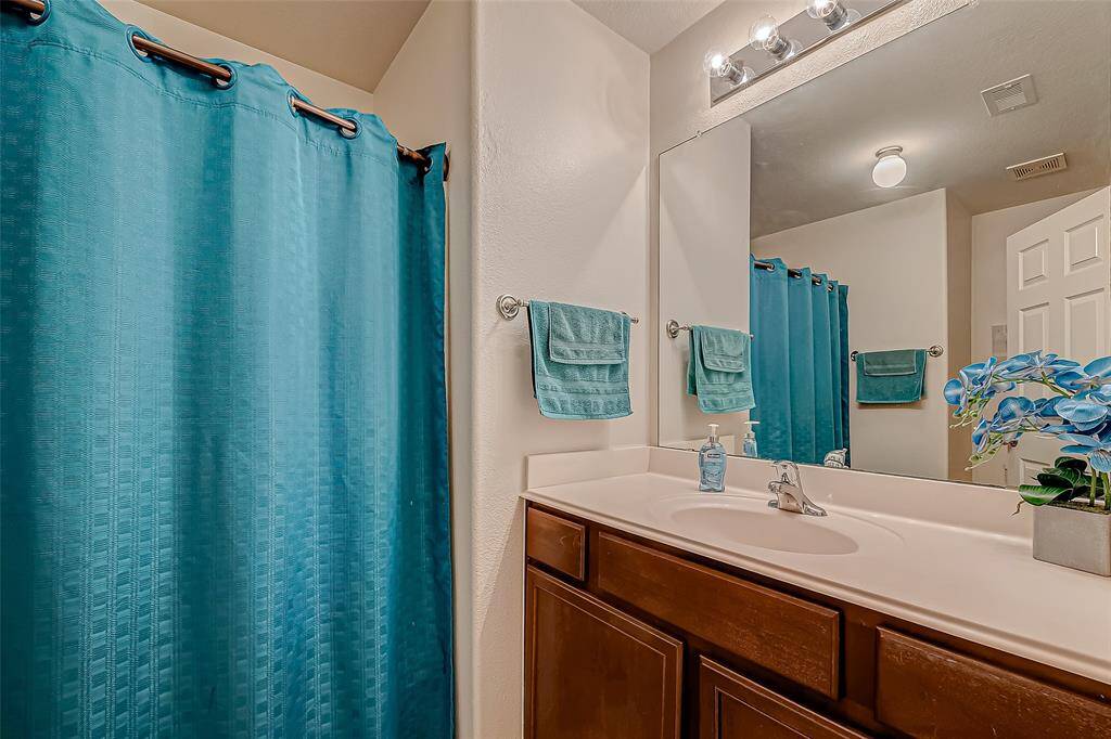This bathroom features a clean and modern design with a large mirror above a single sink vanity with dark wood cabinets. The space is accented by teal towels and a matching shower curtain, providing a pop of color. Bright lighting and a small decorative plant complete the look.
