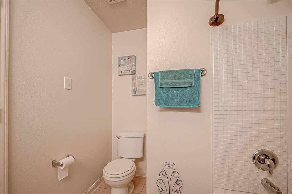 This is a simple, clean bathroom with neutral walls, a tiled shower area, and a standard toilet. It features modern fixtures and a towel rack with a teal towel for a pop of color.