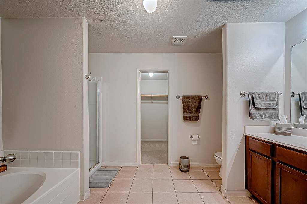This photo showcases a spacious bathroom featuring a bathtub, a separate shower, dual sinks with a large mirror, and a walk-in closet. The neutral tile flooring and walls create a clean and modern look.