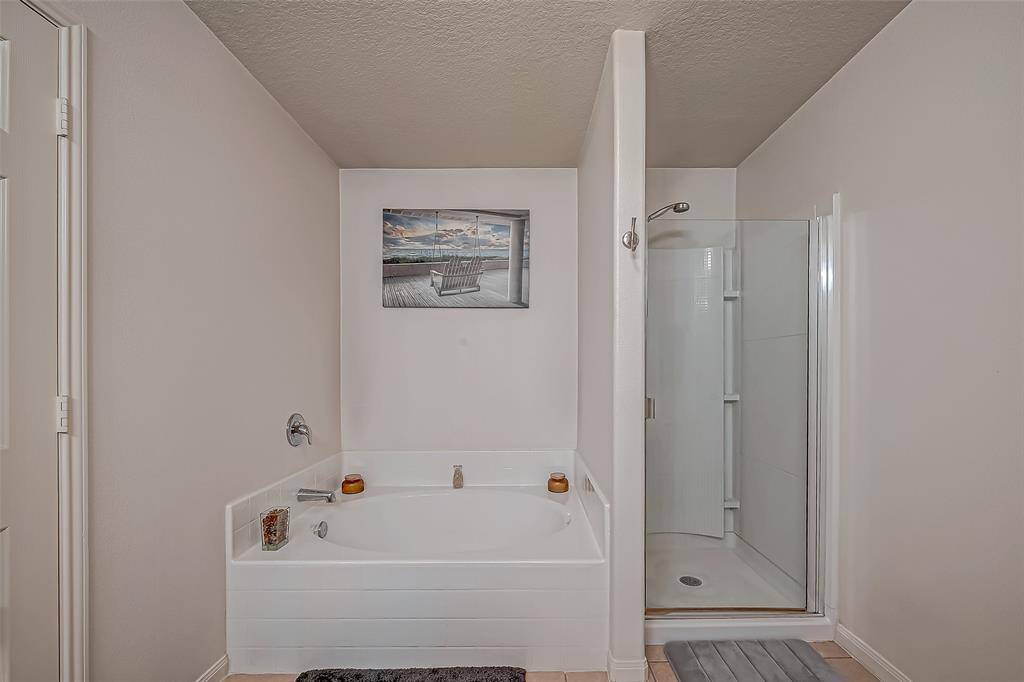This bathroom features a cozy corner bathtub and a separate glass-enclosed shower. The neutral color palette and simple decor create a clean, relaxing atmosphere.