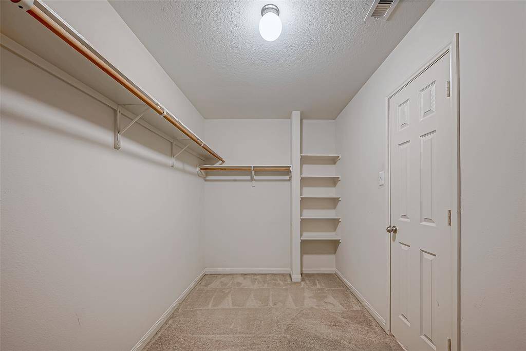 Spacious walk-in closet with ample hanging space and built-in shelves for storage, featuring clean, neutral walls and carpeted flooring.