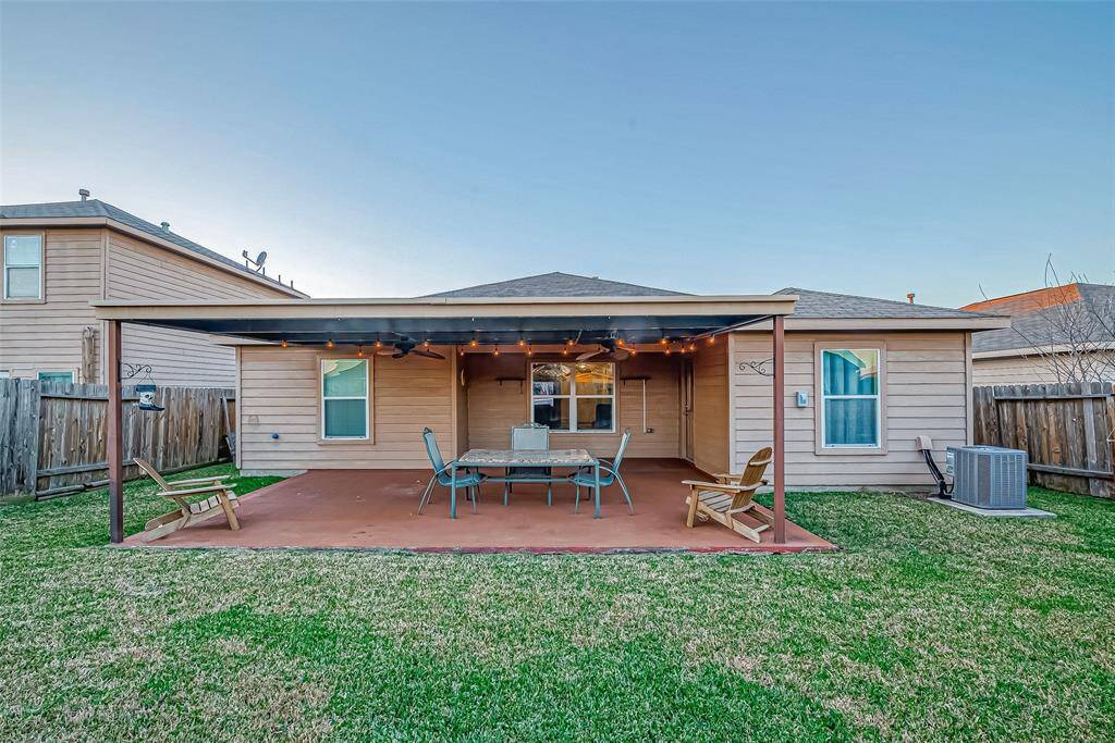 This backyard features a covered patio with outdoor seating, perfect for relaxing or entertaining. The space is surrounded by a wooden fence, providing privacy. The lawn is well-maintained, offering a great area for outdoor activities.