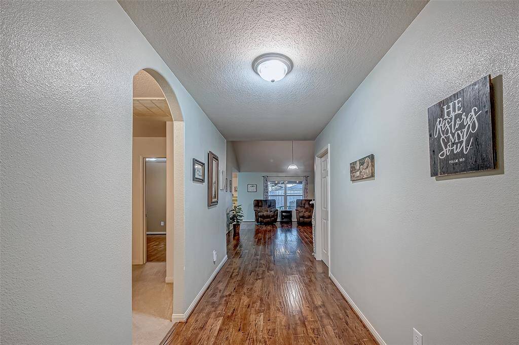 Open the front to this welcoming, wide, well-lit hallway with attractive wood flooring. The space features a stylish archway leading to additional rooms. The end of the hall opens up to a cozy living area with large windows.
