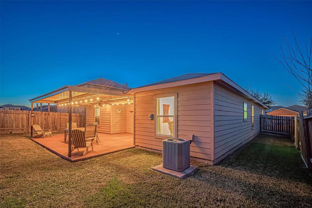 This photo showcases a cozy backyard with a covered patio, adorned with string lights, ideal for evening relaxation. The lawn is well-maintained, and the area is enclosed by a wooden fence, offering privacy and charm.