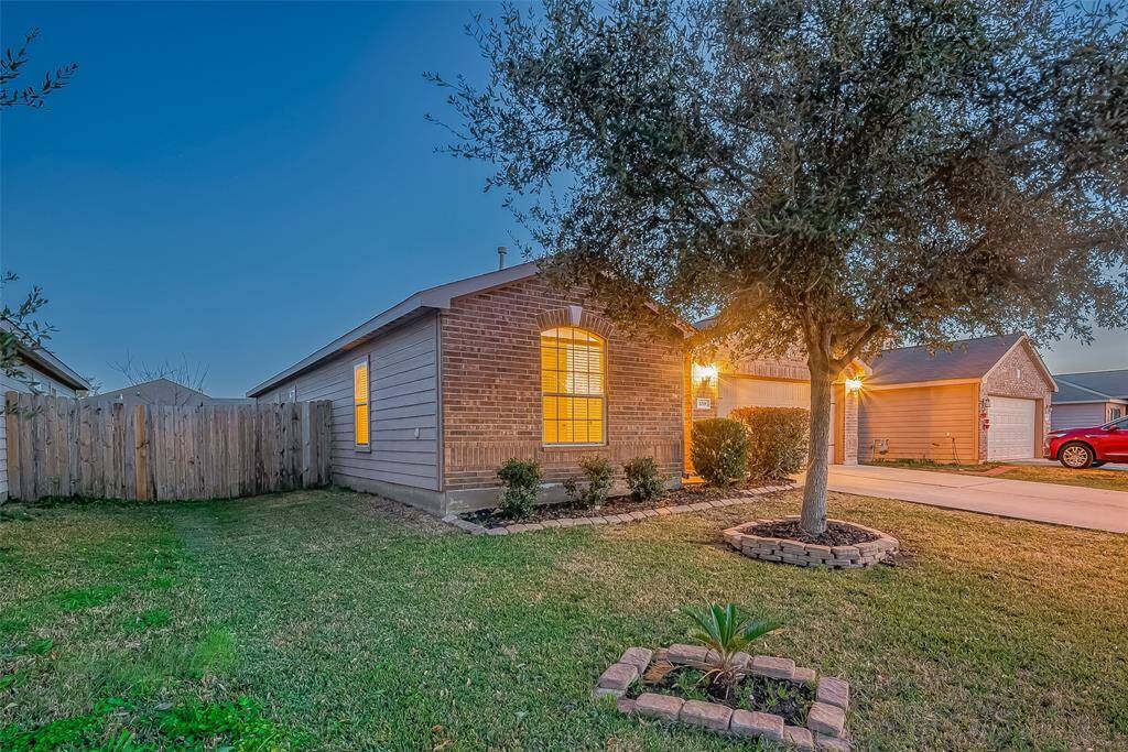 This charming home features a brick facade with warm lighting, a neatly maintained front yard with a tree and small garden bed, and a fenced backyard. The driveway leads to an attached garage, providing convenient parking.