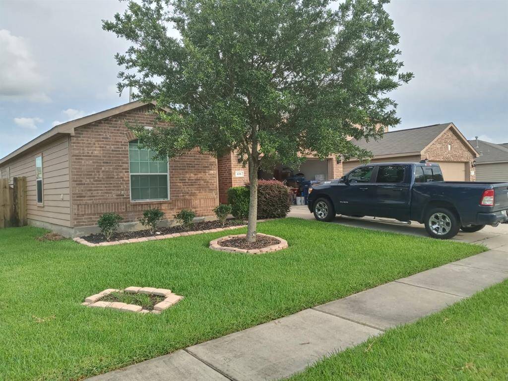 This photo showcases a charming single-story brick home with a neatly landscaped front yard, featuring a mature tree and a driveway with a parked truck. The house has a welcoming appearance, with a well-maintained lawn and flower beds.