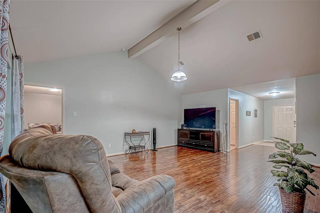 This living room features a vaulted ceiling and gorgeous floors, providing a spacious and inviting atmosphere. Natural light brightens the space, and there's easy access to adjacent rooms and the entryway.