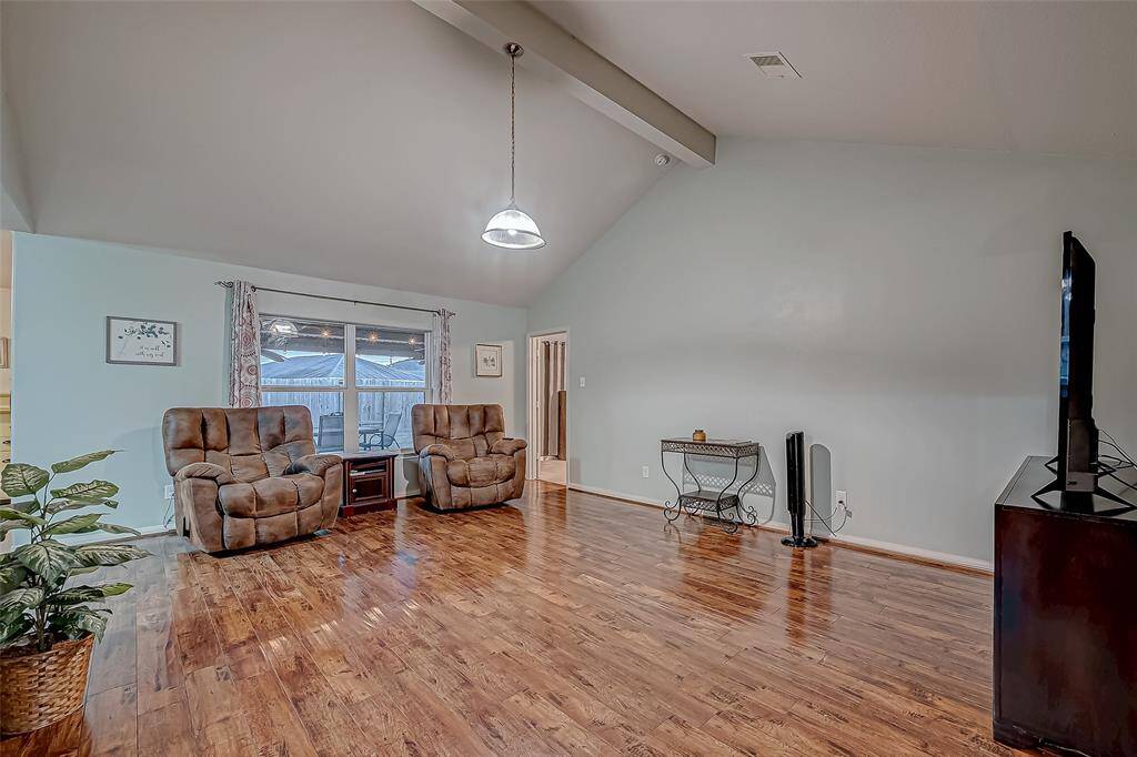 This spacious living room features high vaulted ceilings, beautiful floors, and ample natural light from a large window making it ideal for relaxation.