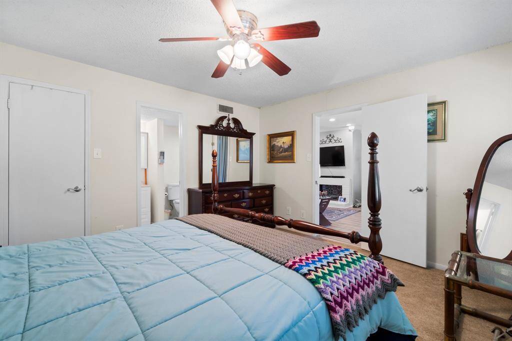 Primary bedroom with a ceiling fan, soft carpet, and ample natural light, and an open door leading to a living area with a fireplace.
