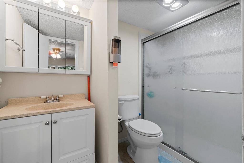This bathroom features a clean, modern design with a spacious shower enclosed by frosted glass doors, a white vanity with a mirrored cabinet, and neutral flooring.