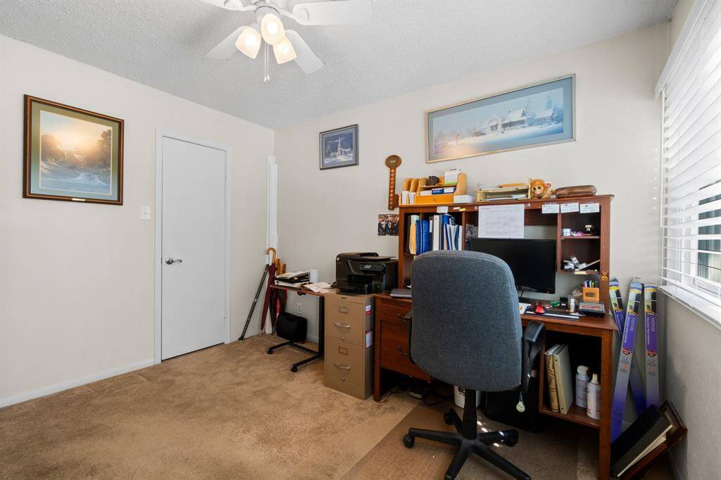 The 2nd bedroom is set up as a cozy home office with a desk, chair, and storage. It features carpeted flooring, a ceiling fan, and ample natural light from a window, making it an ideal workspace.