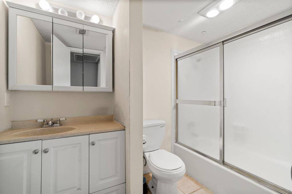 This bathroom features a clean, modern design with a mirrored cabinet above a single sink vanity, a toilet, and a bathtub with sliding glass doors.