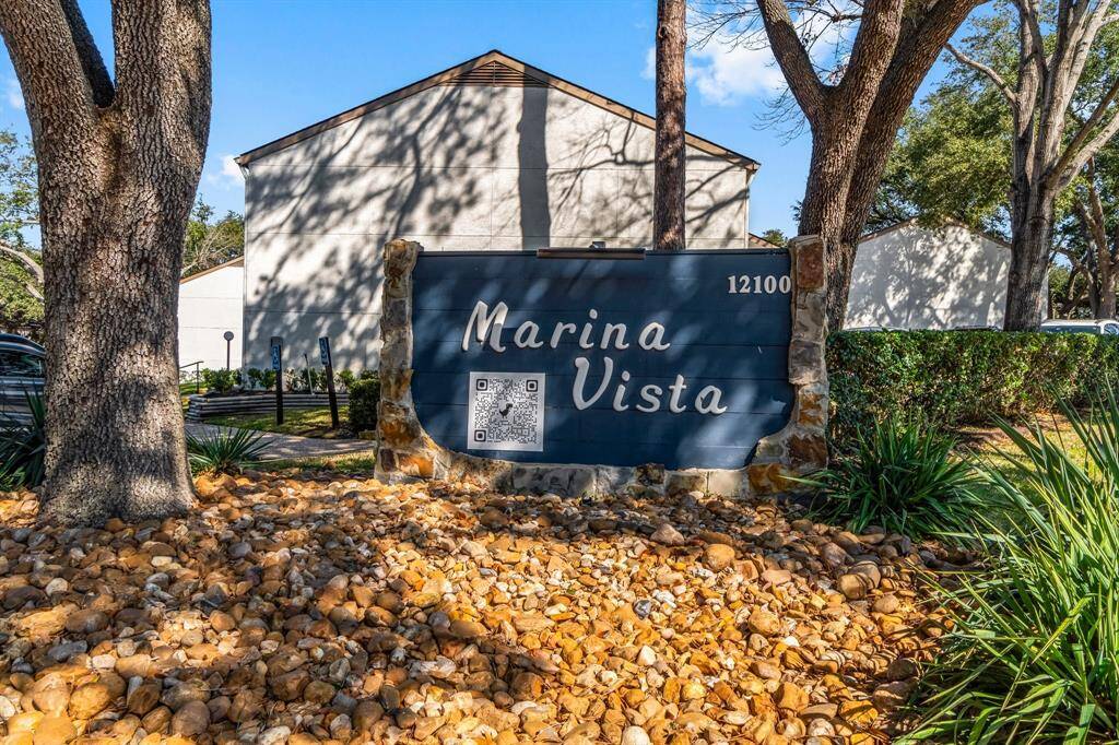 This photo shows the entrance sign for "Marina Vista," a residential community. The sign is set amidst landscaped rocks and greenery, with a backdrop of trees and buildings.