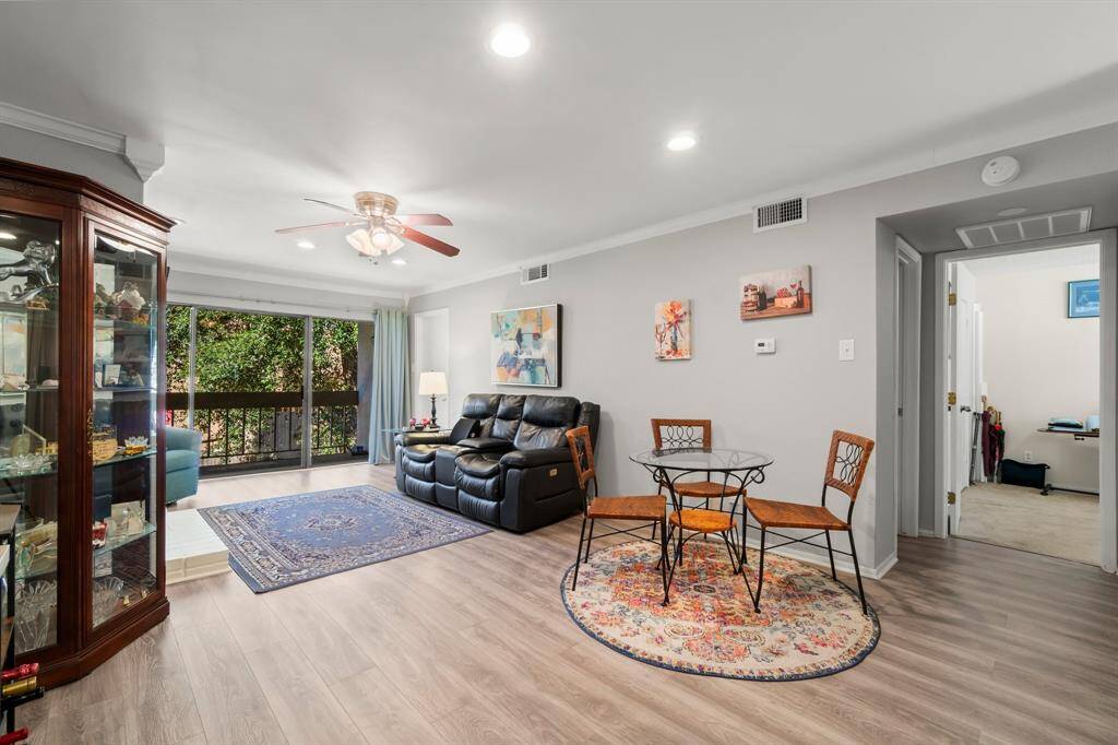 This spacious living area features hardwood floors, a cozy seating arrangement, and large windows offering abundant natural light. The open layout includes a dining area, and there's easy access to adjacent rooms and outdoor views.