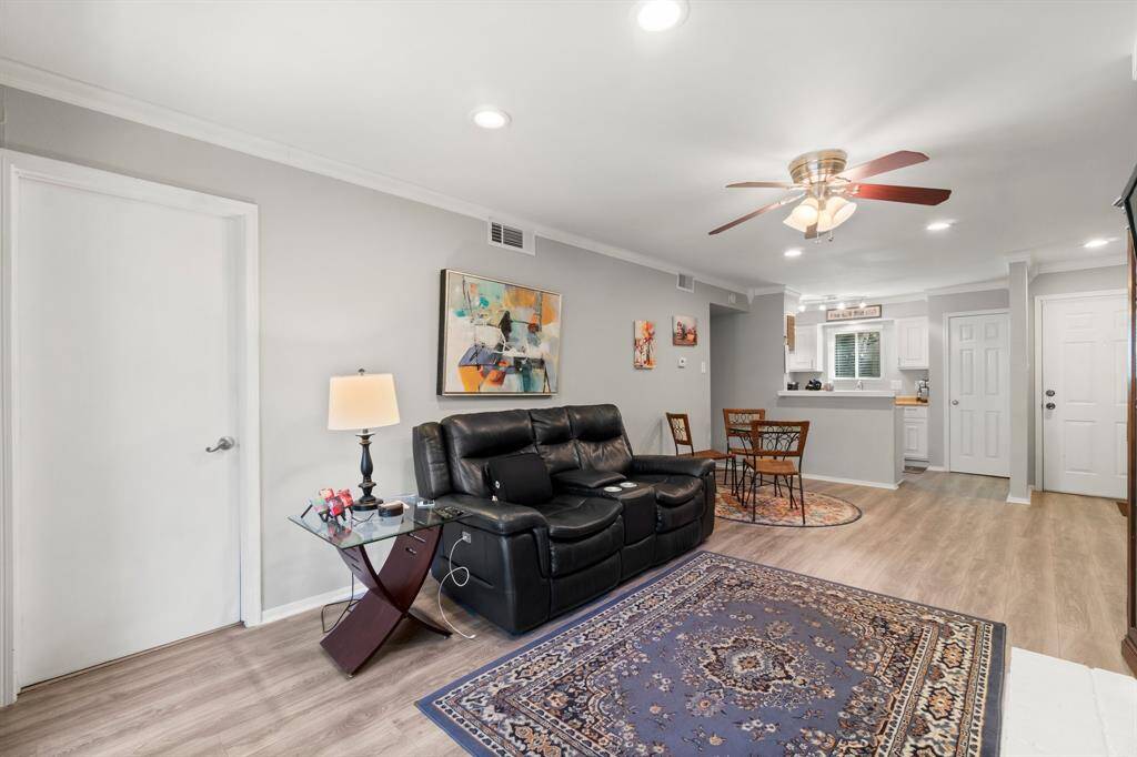 This photo showcases a cozy, modern living area. The open layout includes a dining space with a  bright kitchen. The room is well-lit with recessed lighting and a ceiling fan, and the neutral walls create a welcoming atmosphere.