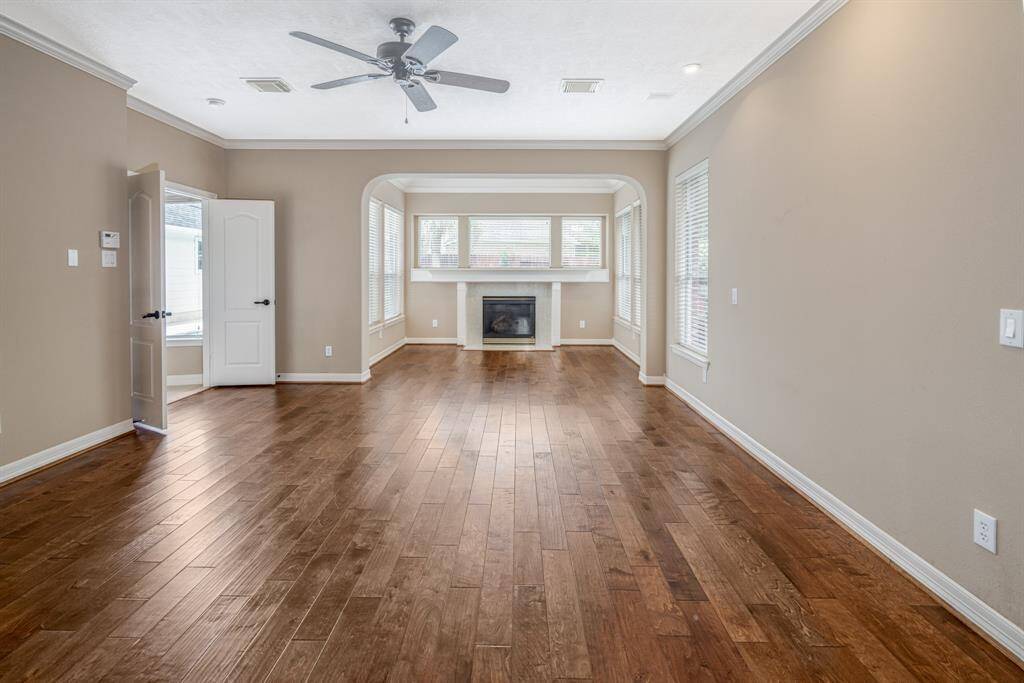 Bright and inviting primary bedroom featuring elegant hardwood floors, a cozy fireplace, and abundant natural light from large windows. Perfect for relaxing or entertaining.
