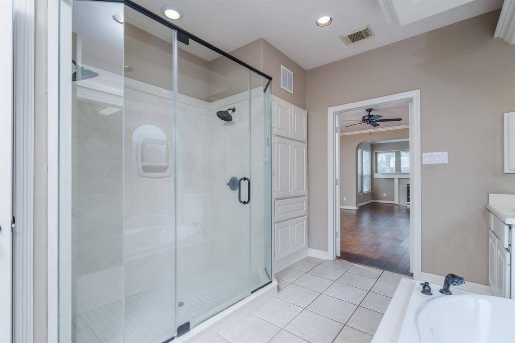 Experience luxury in this modern primary bathroom featuring a spacious glass-enclosed shower and elegant tile flooring. The open design seamlessly connects to a cozy living area with rich wood flooring, creating a perfect blend of comfort and style.