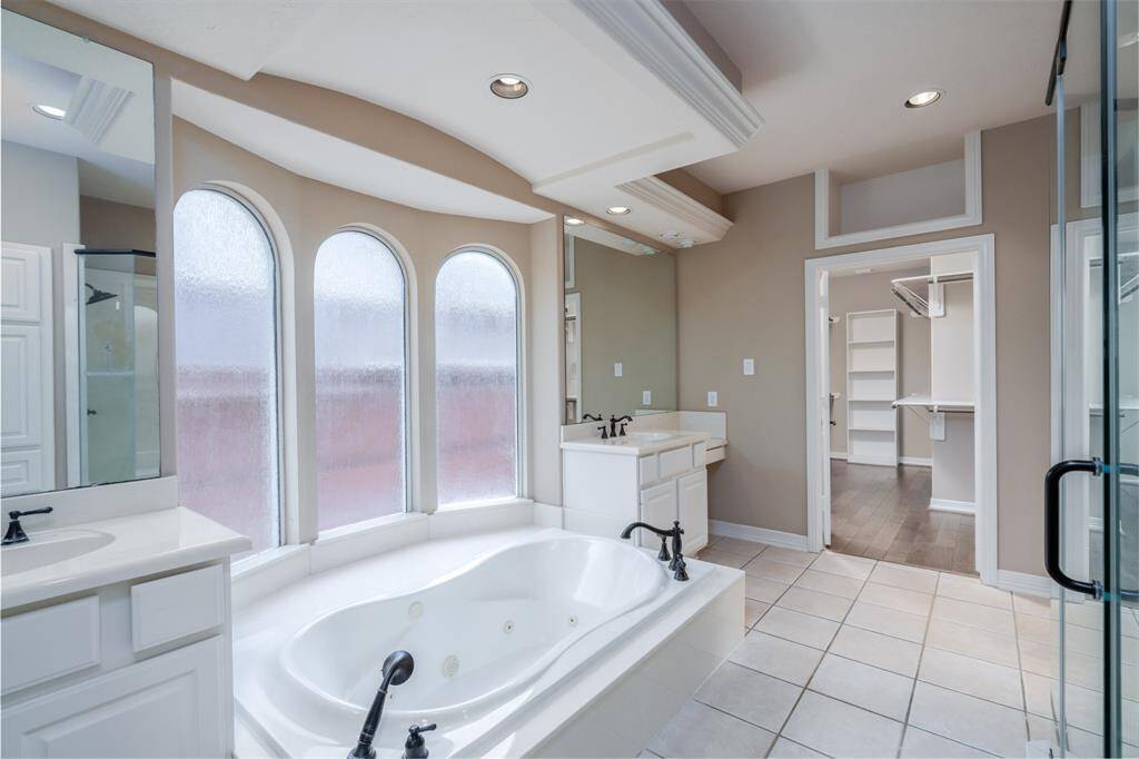 Luxuriate in this elegant bathroom featuring a spacious soaking tub, dual vanities, and abundant natural light from arched windows. Enjoy seamless flow into a generously sized walk-in closet.