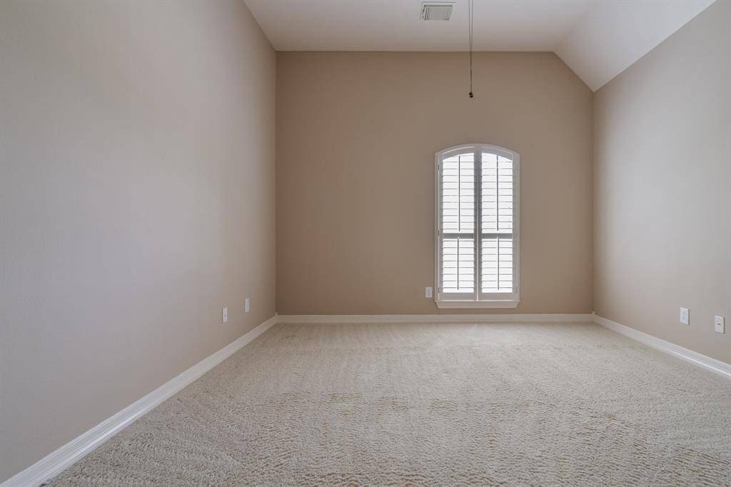 Bright and airy room with high ceilings and a large window featuring elegant shutters. Neutral walls and plush carpeting create a warm and inviting space, perfect for a bedroom or home office.