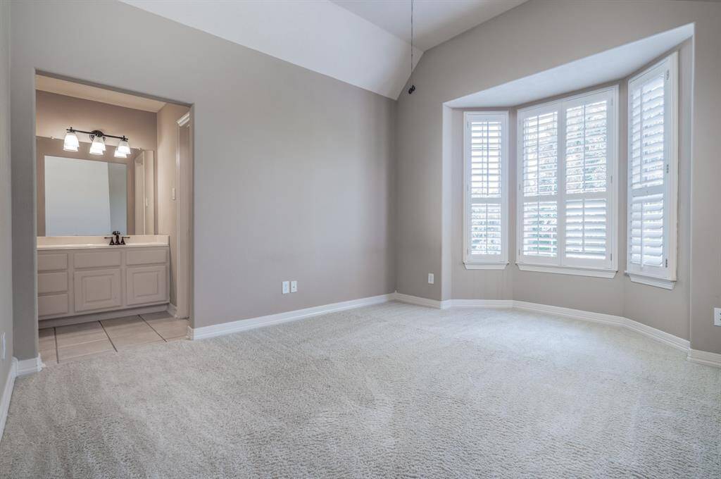This bright, cozy bedroom features elegant bay windows with plantation shutters and an ensuite vanity area, perfect for comfort and convenience.