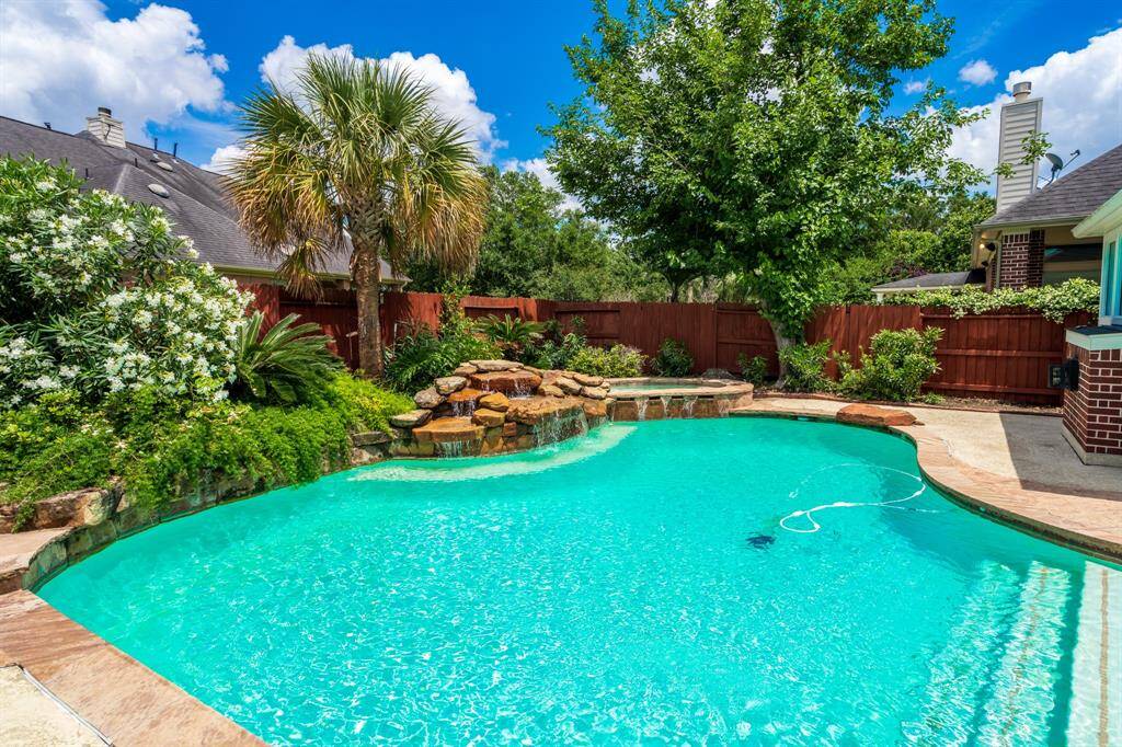 This inviting backyard features a sparkling pool with a rock waterfall, lush landscaping, and a private wood fence, creating a perfect oasis for relaxation and entertaining.
