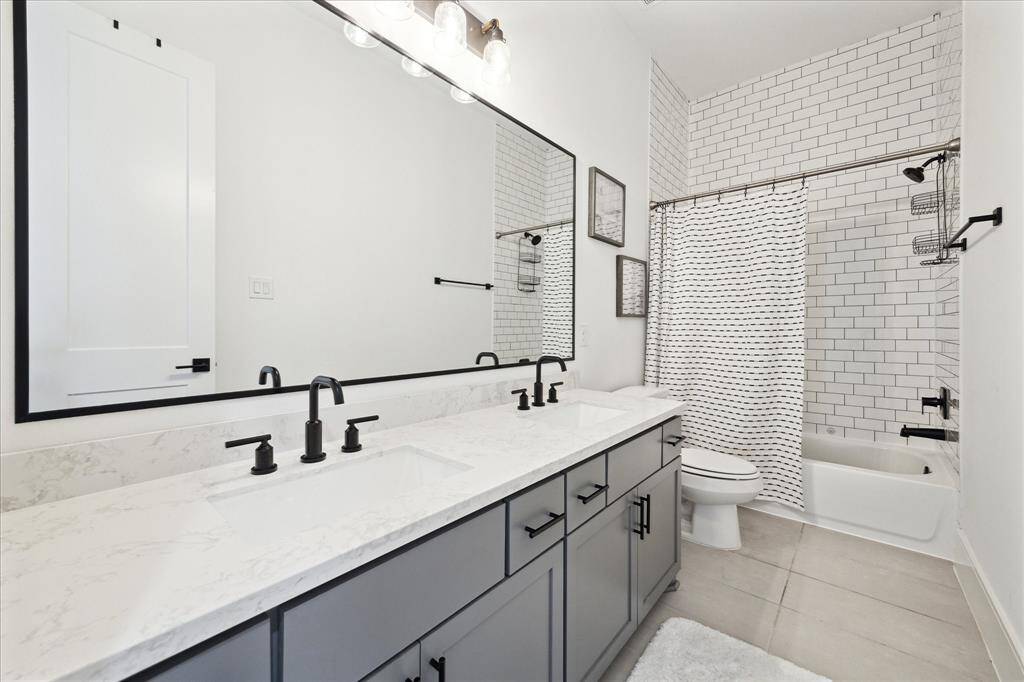 Secondary bathroom with double vanity, plenty of storage, tub/shower combo, large framed mirror and sleek tiles.