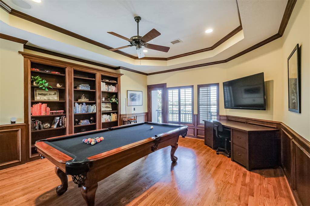 Welcome to the billards room! Notice how the tray ceiling, with it's elegant crown molding, hardwood flooring and built-in shelving,  accentuate the luxurious styling of the room. The door in the back leads to a balcony with views of the pool and lake.