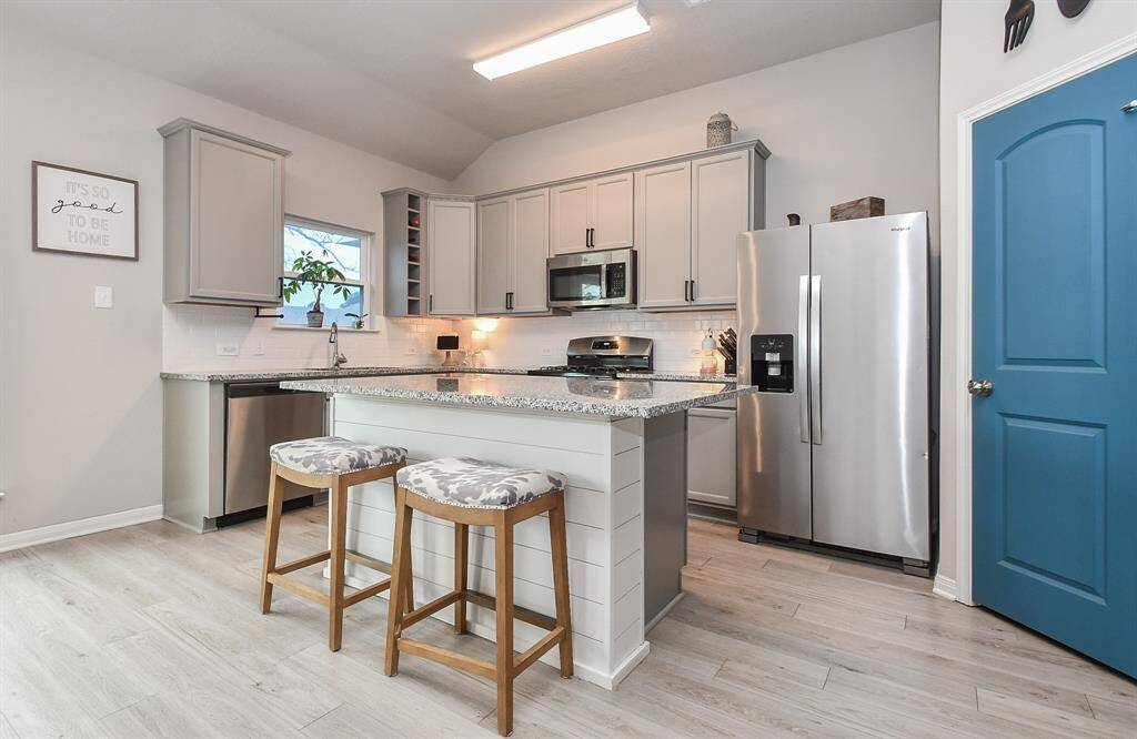 The space features light gray cabinetry with black hardware, stainless steel appliances, and a white subway tile backsplash.