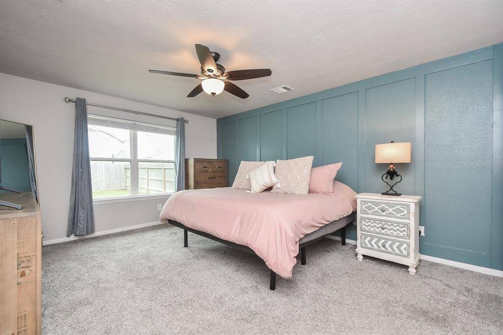 Primary bedroom features a accent wall with elegant paneling. The neutral-toned carpet and light gray walls create a calming ambiance.