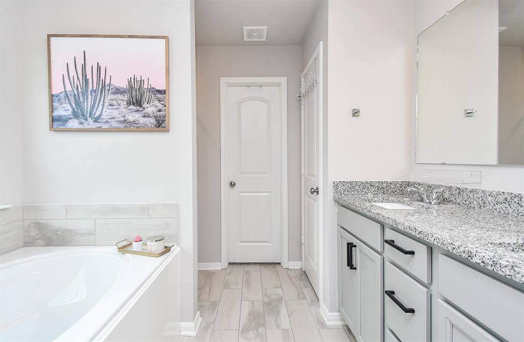 En suite primary bathroom with a clean and elegant design. The space features a separate tub and shower, sleek gray vanity with granite countertop and black hardware.
