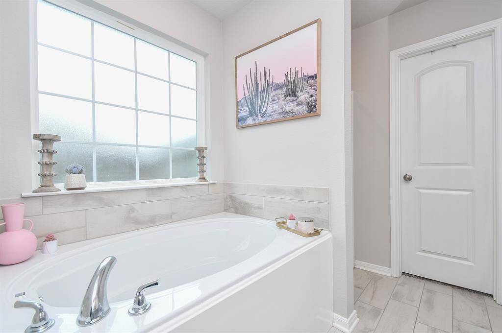 Luxurious bathroom with a large soaking tub positioned beneath a frosted window, allowing natural light to enter while maintaining privacy.