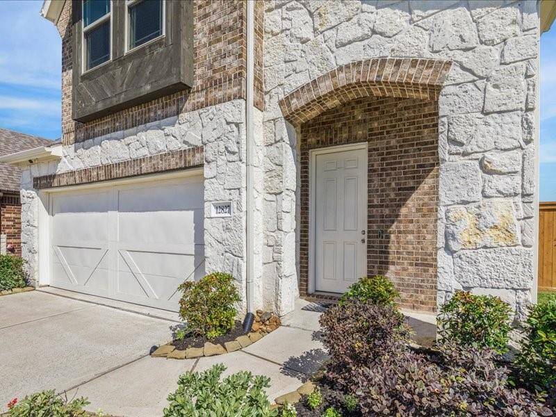 Charming home exterior featuring a two-car garage and a welcoming front entrance framed by elegant stone and brickwork. Well-maintained landscaping adds curb appeal to this inviting property.