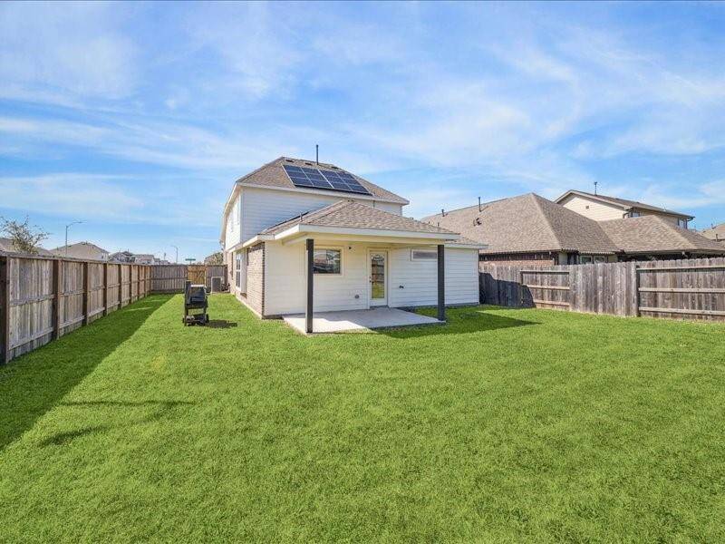 This photo shows a two-story house with solar panels and a spacious fenced backyard. The house features a covered patio, providing a perfect outdoor space.