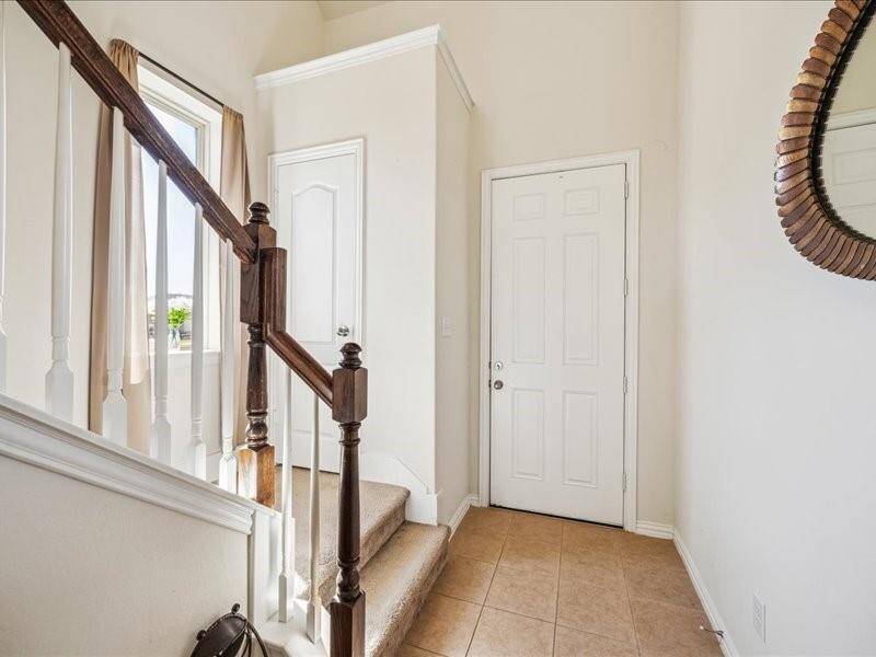 This entryway features a tiled floor, a staircase with wooden banisters, and window for natural light.