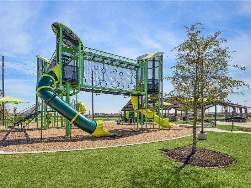 This photo features a modern playground with vibrant green and yellow climbing structures, slides, and swings set on a well-maintained grassy area. It's an inviting outdoor space ideal for families.