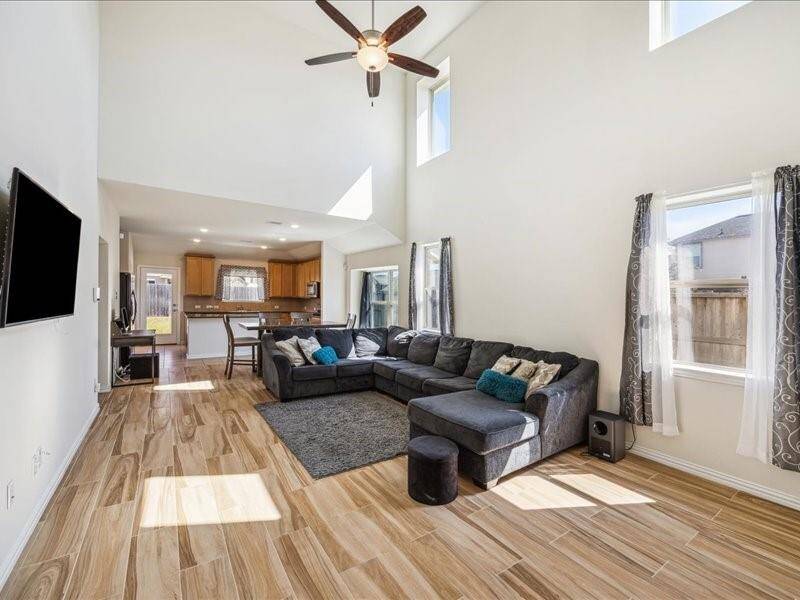This bright, open-concept living area features high ceilings, large windows, and wood-look flooring, and a view into the kitchen that is perfect for family gatherings and entertaining.