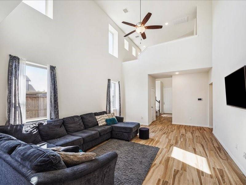 This bright, open-concept living area features high ceilings, large windows, and wood-look flooring, and a view into the kitchen that is perfect for family gatherings and entertaining.