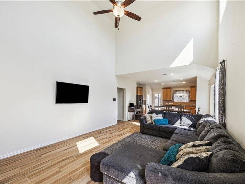 This bright, open-concept living area features high ceilings, large windows, and wood-look flooring, and a view into the kitchen that is perfect for family gatherings and entertaining.