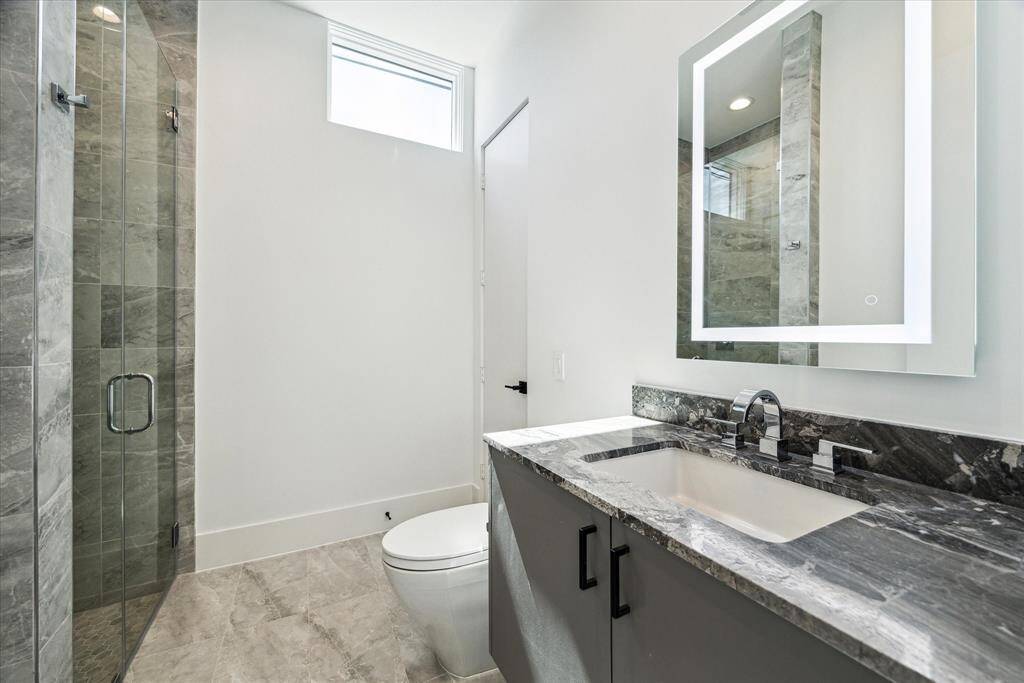The guest suite's full bath showcases a Quartzite-topped vanity with ample storage, an LED-lit vanity mirror, and a glass-enclosed walk-in shower